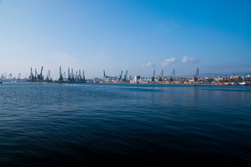 Fototapeta na wymiar Morning port pier with crane and infrastructure for shipping industry, cargo transportation dock with blue water and clear sky. City export and import harbor with warehouses.