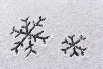 Two snowflakes are painted on a snow cover. Black pattern of snowflakes on white snow.