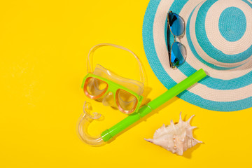 Top view on beach accessories on yellow background - sunglasses and striped blue hat, diving mask and shell. Concept of the long-awaited vacation at sea and travel. Advertising space