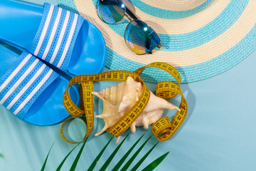 Top view of striped hat, sunglasses, measuring tape with a seashell and a palm branch on a turquoise blue background. Concept of losing weight for a vacation at sea. Advertising space