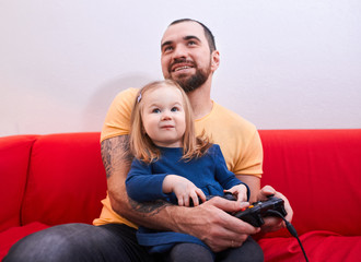 happy caucasian father with beard sit with sweet daughter playing video games holding joysticks,...