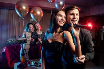 smiling cute young caucasian couple spend free time, celebrating in karaoke bar, man and woman in black wear singing together in microphone, look side