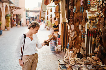 Travel and shopping. Young traveling woman with choose presents in shoes shop in Morocco.