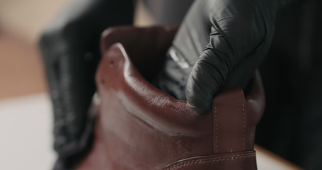 man hands in black gloves applying protective cream to brown leather sneakers