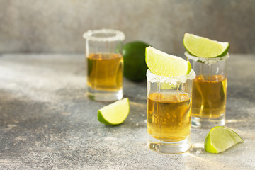 Gold Tequila. Mexican Gold Tequila shot with lime and salt on a stone light concrete worktop.