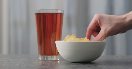 man hand take potato chips with plack pepper from white bowl on concrtete countertop