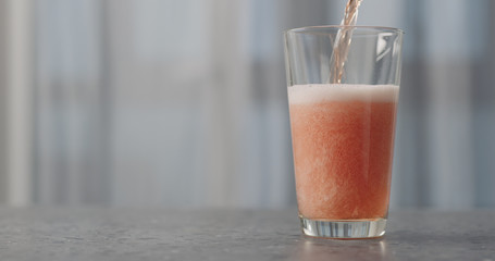 pour orange fizzy drink into pint glass on concrete countertop with copy space