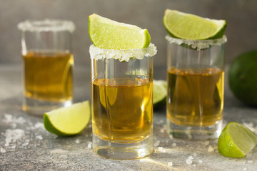 Gold Tequila. Mexican Gold Tequila shot with lime and salt on a stone light concrete worktop.