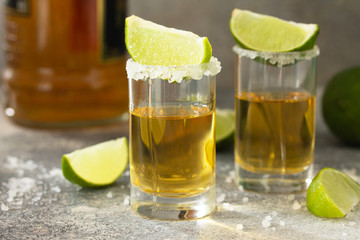 Gold Tequila. Mexican Gold Tequila shot with lime and salt on a stone light concrete worktop.