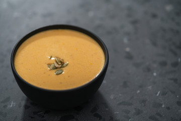 Pumpkin cream soup with pumpkin seeds in a black bowl on concrete background