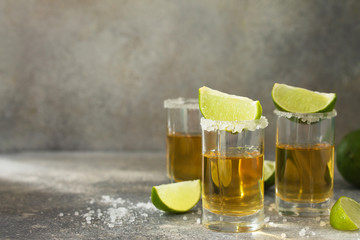Gold Tequila. Mexican Gold Tequila shot with lime and salt on a stone light concrete worktop. Copy space.