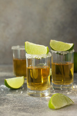Gold Tequila. Mexican Gold Tequila shot with lime and salt on a stone light concrete worktop.