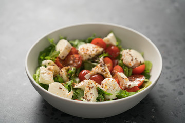 Salad with cherry tomatoes, mozzarella and frisee leaves in white bowl on concrete background