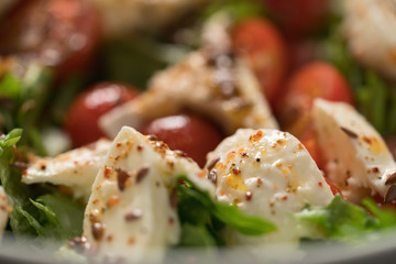 Closeup salad with cherry tomatoes, mozzarella and frisee leaves in white bowl on concrete...