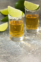Fototapeta na wymiar Gold Tequila. Mexican Gold Tequila shot with lime and salt on a stone light concrete worktop. Copy space.