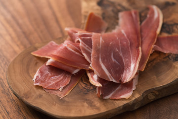 sliced prosciutto on olive wood board