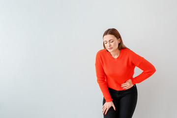 Young woman suffering from abdominal pain on grey background