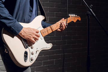 Young man playing guitar near dark brick wall