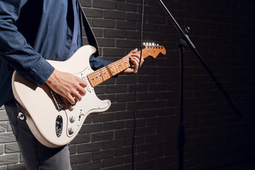 Young man playing guitar near dark brick wall