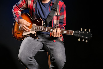 Young man playing guitar on dark background