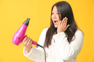 Surprised Asian woman with hair dryer on color background