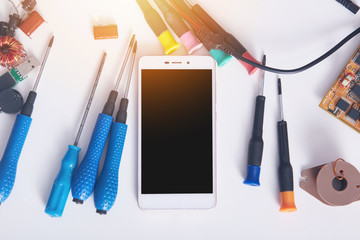 Picture of modern smart phone with black blank screen for copy space for advertisment or promotion. Faulty mobile phone in electronic smart phone technology service on white surface near screwdrivers.