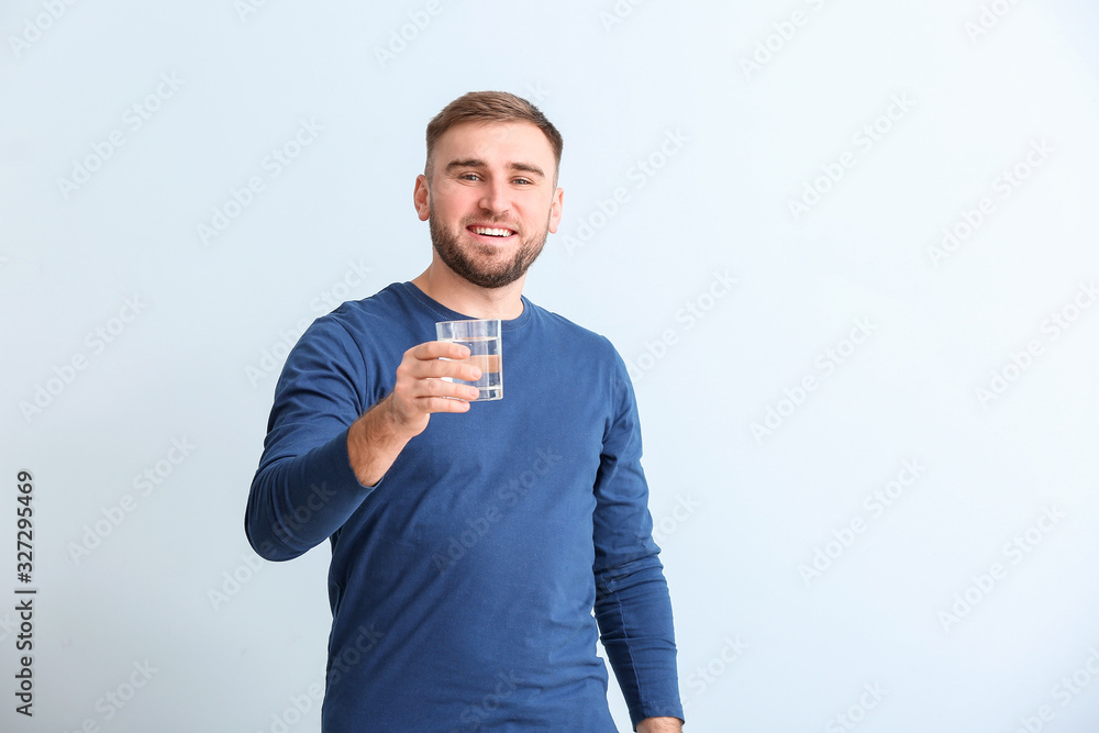 Poster Young man with glass of water on light background