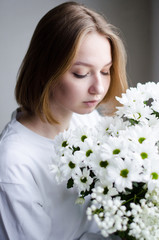 portrait of a young beautiful girl with blond hair and a short haircut with white flowers in her hands on a white background, the concept of beauty and health