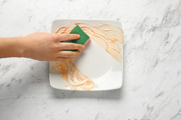 Woman washing dirty empty plate on light background