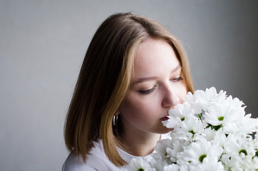 Obraz na płótnie Canvas portrait of a young beautiful girl with blond hair and a short haircut with white flowers in her hands on a white background, the concept of beauty and health