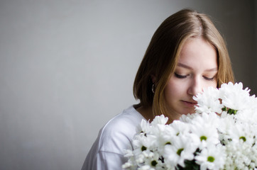 portrait of a young beautiful girl with blond hair and a short haircut with white flowers in her hands on a white background, the concept of beauty and health