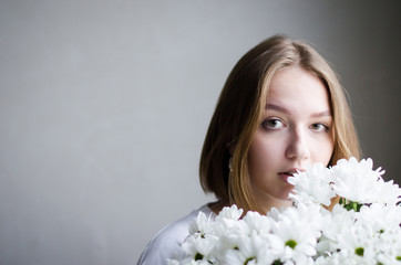 portrait of a young beautiful girl with blond hair and a short haircut with white flowers in her hands on a white background, the concept of beauty and health