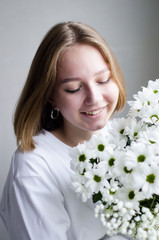 portrait of a young beautiful girl with blond hair and a short haircut with white flowers in her hands on a white background, the concept of beauty and health