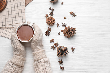 Female hands with cup of hot chocolate on white wooden background