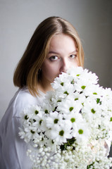 portrait of a young beautiful girl with blond hair and a short haircut with white flowers in her hands on a white background, the concept of beauty and health