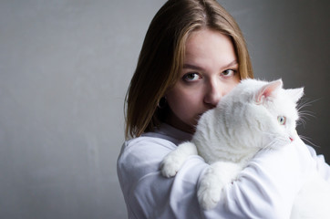 portrait of a young beautiful girl in a white sweater on a white background with a cute white cat in her arms. Kitten enjoys being in girls arms.