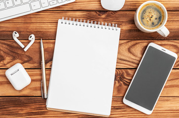 Notepad with smartphone, wireless headphones, cup of coffee and computer keyboard on wooden desk. Top view.