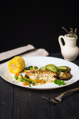 fried white sea fish with vegetables and corn on a dark background