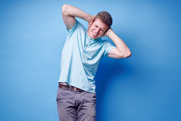 To loud! Young man closes his ears with hands refusing to listen to something. Blue background.
