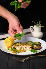 fried white sea fish with vegetables and corn on a dark background