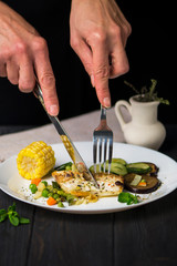 fried white sea fish with vegetables and corn on a dark background