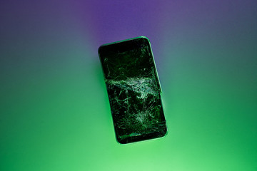 Mobile smartphone with broken screen on green background.