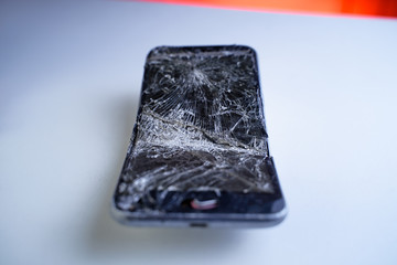 Mobile smartphone with broken screen on white table.
