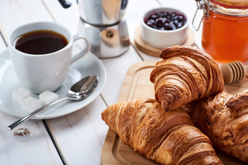 Closeup photo of breakfast or snacks. Croissants with honey and jam, cup of coffee. White wooden table top