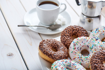 Closeup photo of sweet breakfast or snacks. Chocolate donuts and cup of coffee. White wooden table top