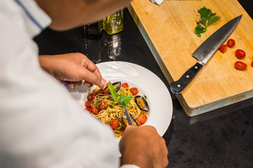 closeup of a chef serving and decorating a plate spaghetti Vongole with roma tomatoes and mussels next to a cutboard and a knife