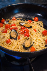 closeup of spaghetti Vongole with roma tomatoes and mussels beeing heated in a pan on a gas stove