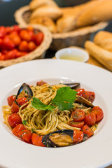 closeup of spaghetti Vongole with roma tomatoes and mussels served and decorated on a plate with tomatoes, bread and olive oil in the background