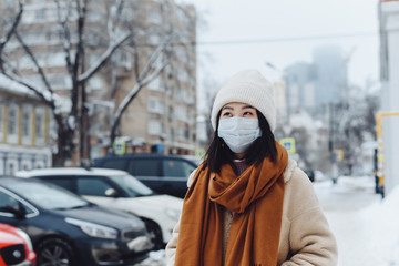 the girl next to the cars and against the background of high-rise buildings looks at the camera in a protective medical mask. The concept of coronavirus in everyday life