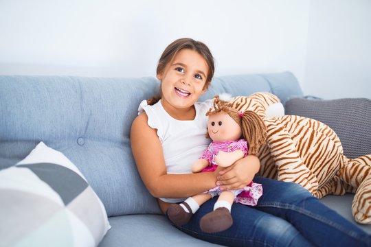 Adorable toddler smiling happy. Sitting on the sofa hugging doll at home
